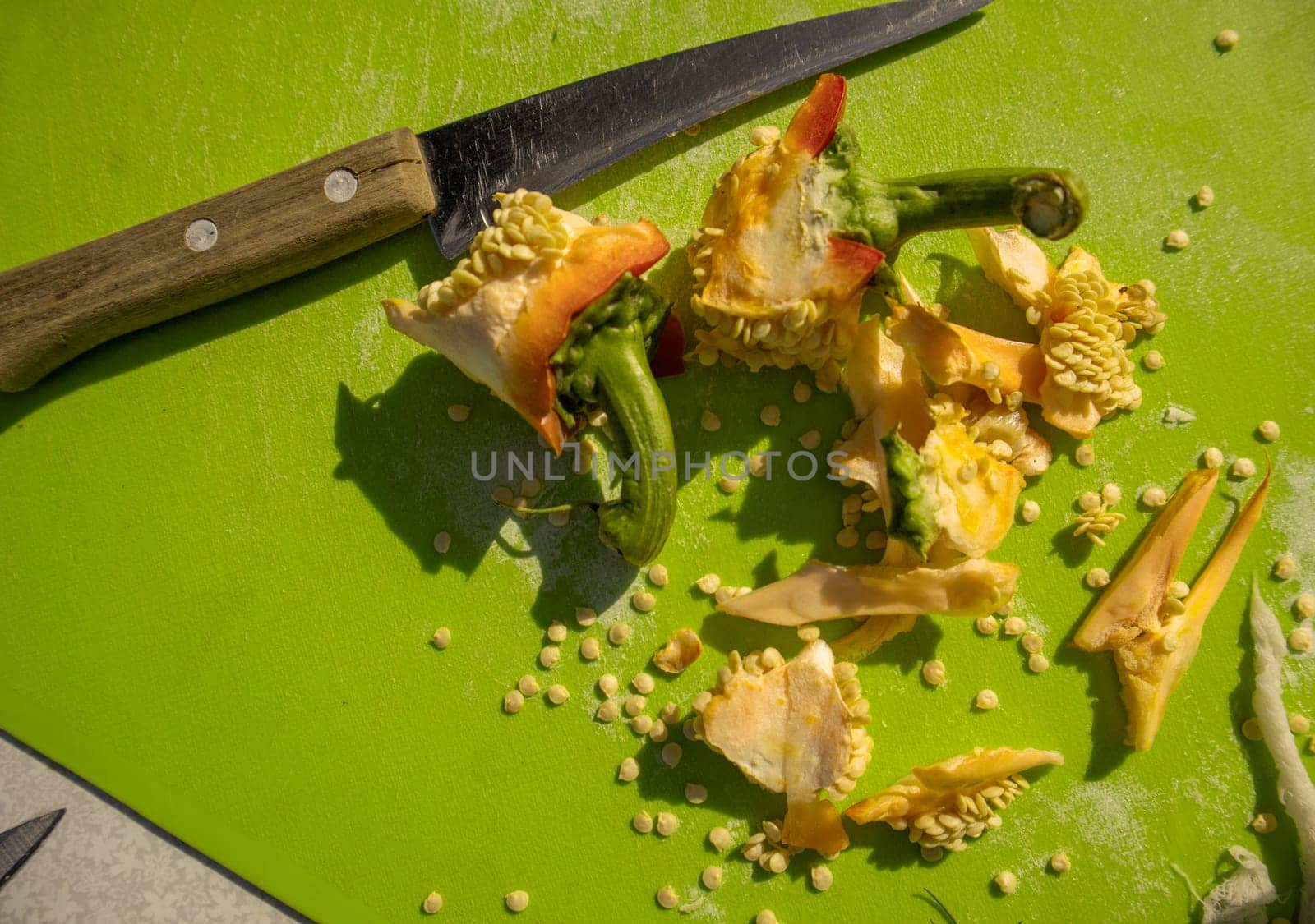 Cooking and cutting sweet peppers, close-up knife, seeds, peel on a green cutting board, top view.