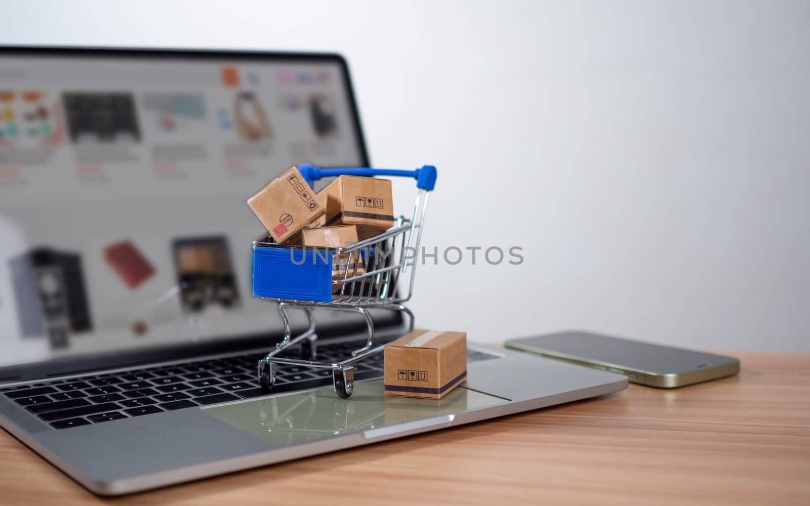Shopping cart and product boxes placed on laptop computer represent online shopping concept, website, e-commerce, marketplace platform, technology, transportation, logistics and online payment concept. by Unimages2527