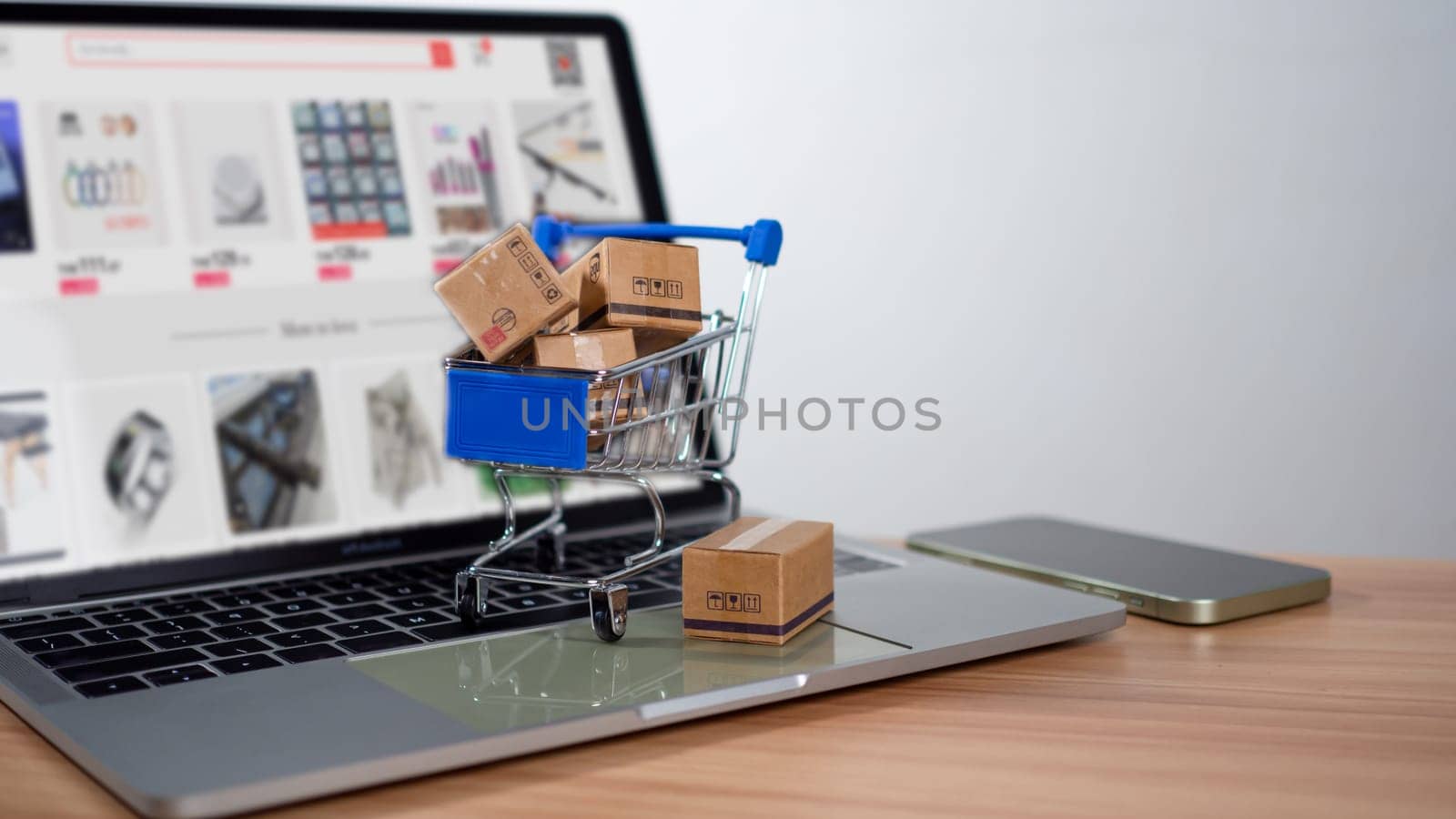 Shopping cart and product boxes placed on laptop computer represent online shopping concept, website, e-commerce, marketplace platform, technology, transportation, logistics and online payment concept. by Unimages2527