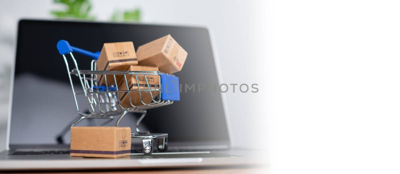 Shopping cart and product boxes placed on laptop computer represent online shopping concept, website, e-commerce, marketplace platform, technology, transportation, logistics and online payment concept. by Unimages2527