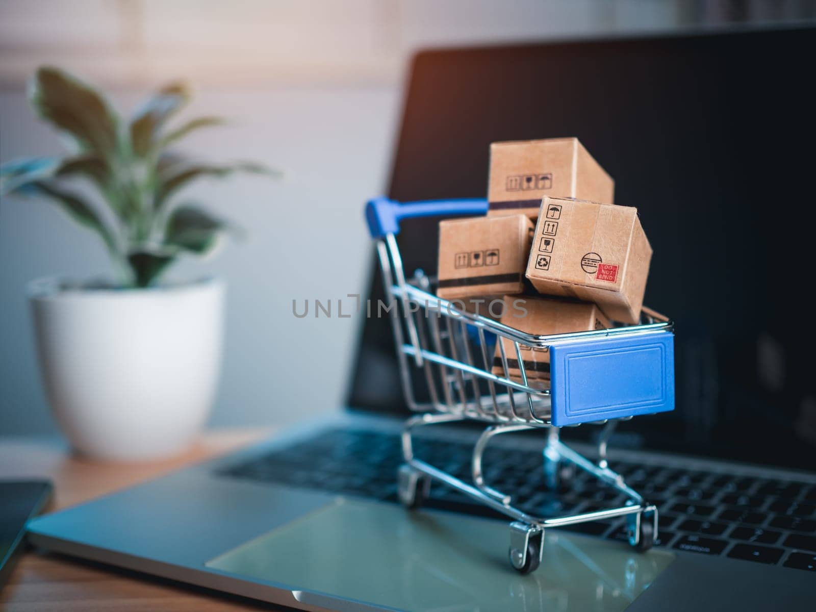 Shopping cart and product boxes placed on laptop computer represent online shopping concept, website, e-commerce, marketplace platform, technology, transportation, logistics and online payment concept.