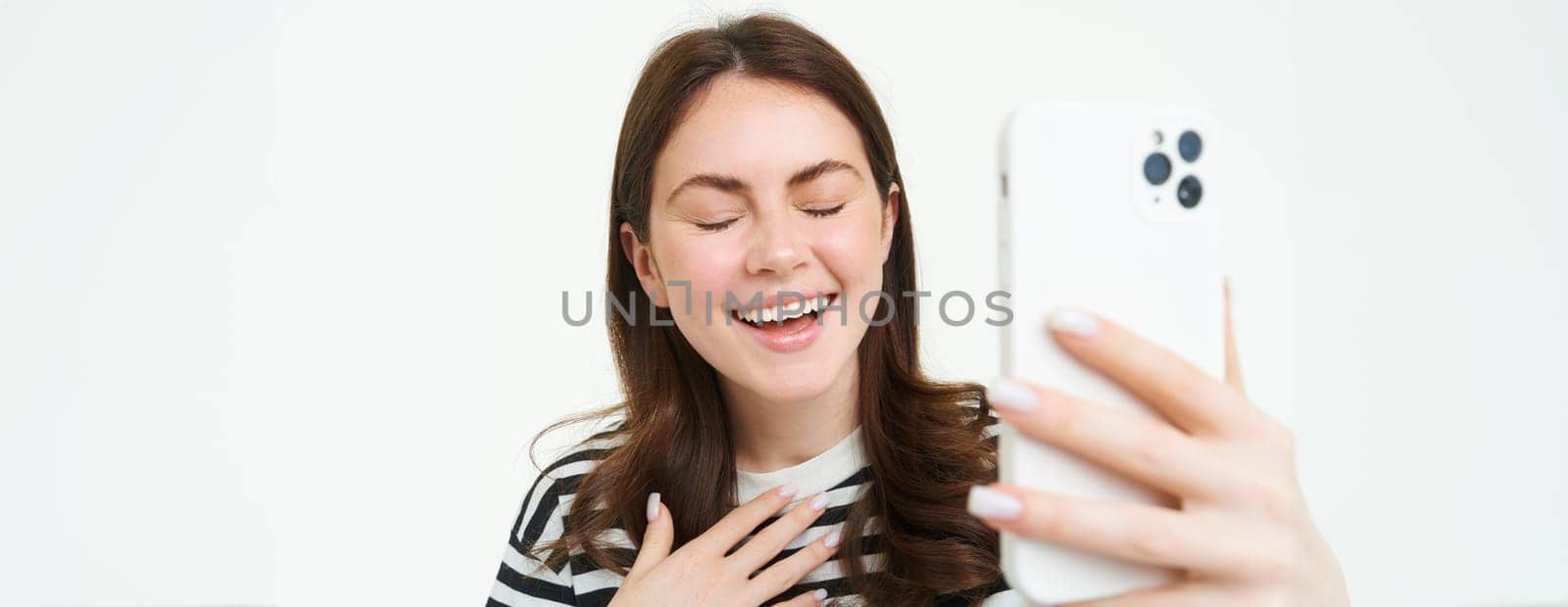 Portrait of woman laughing while taking selfie with funny photo filters, standing over white isolated background.