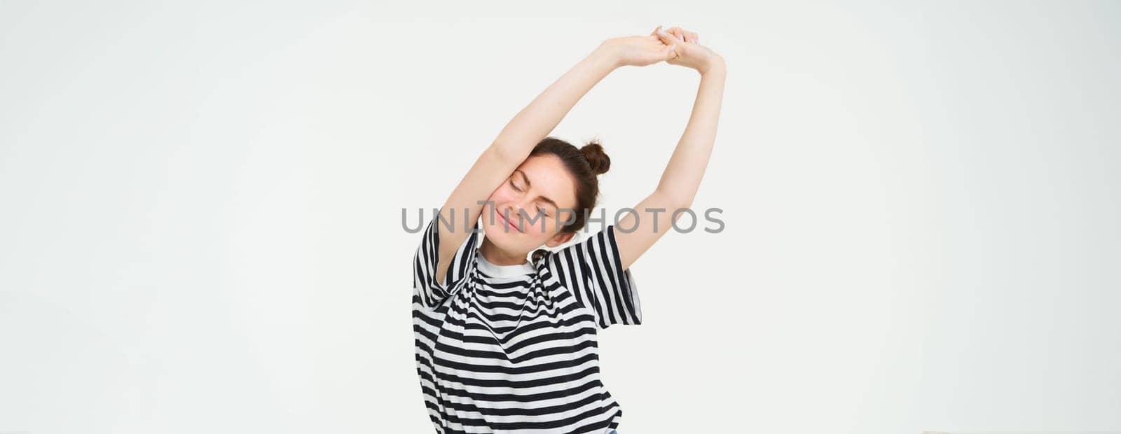 Portrait of happy young woman, stretching arms with pleased smile after good nap, standing over white background.