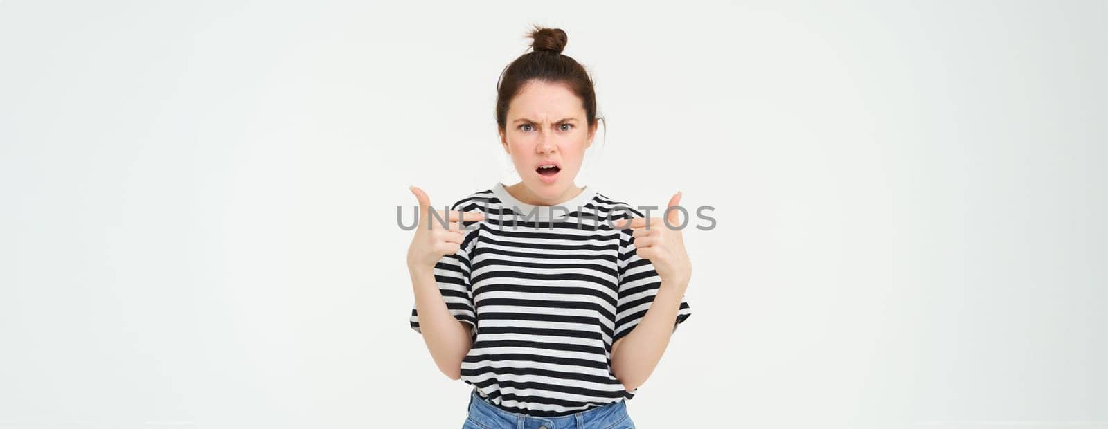 Annoyed woman pointing at herself and frowning, arguing, looking frustrated and disappointed, shouting, standing over white background by Benzoix