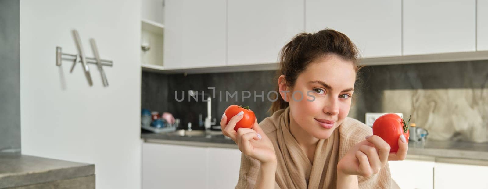 Portrait of beautiful woman cooking in the kitchen, chopping vegetables on board, holding tomatoes, lead healthy lifestyle with preparing fresh salads, vegan meals by Benzoix