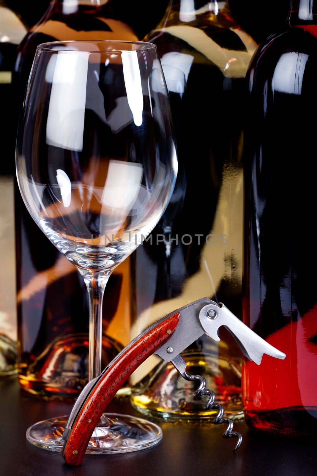 Wine glass,corkscrew with precious wood handle and wine bottles against a black background