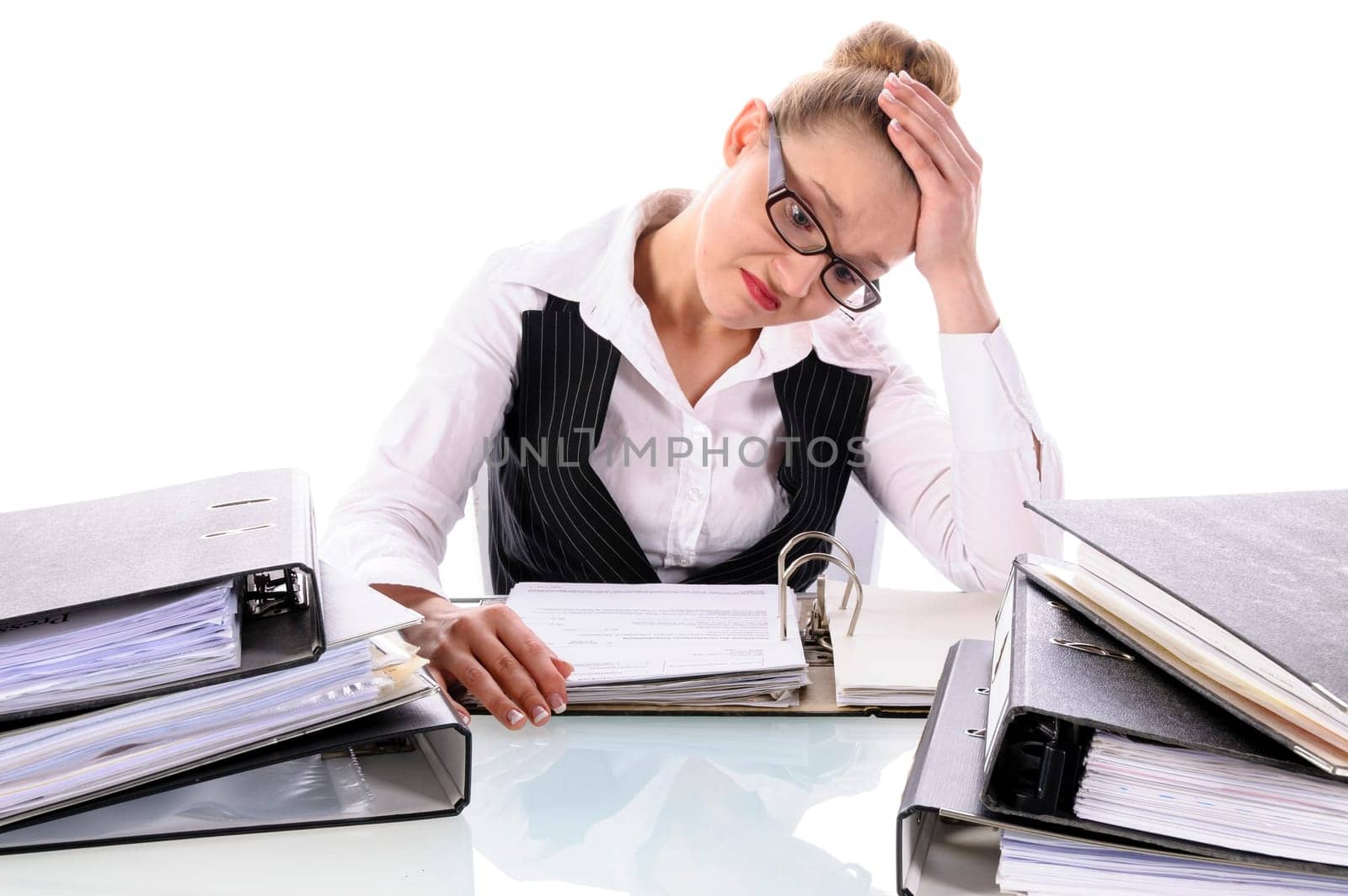 Young woman with blond hair in a business suit (tax consultant,manager,secretary) sits at her desk and pores over a stack of files against a white background.