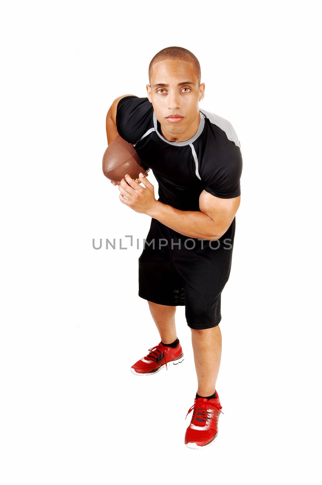 A young Jamaican football player in his black outfit standing for.white background with his football under his arm..