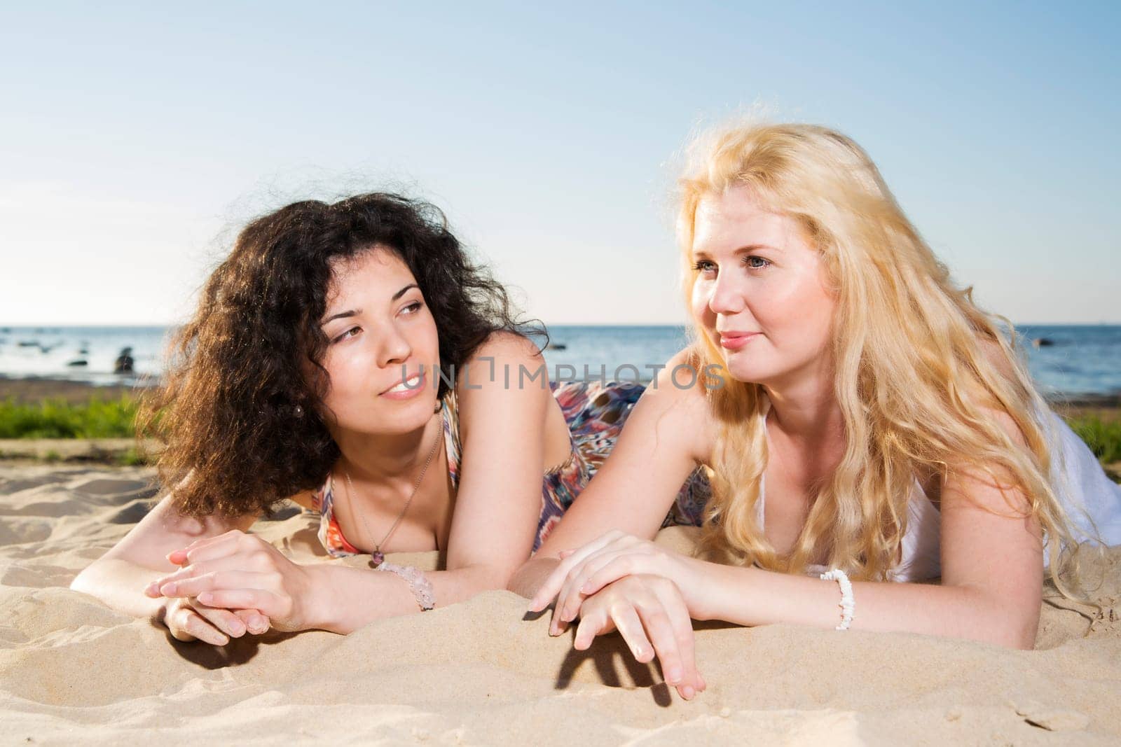 Two young womans lay together at beach sand