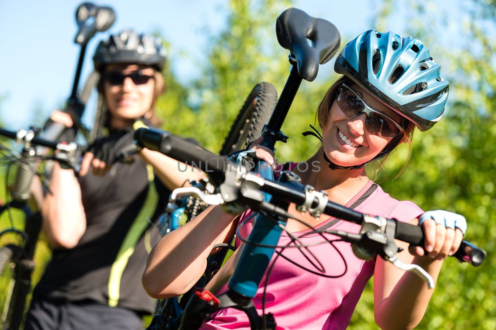 Smiling sporty couple carrying their mountain bikes