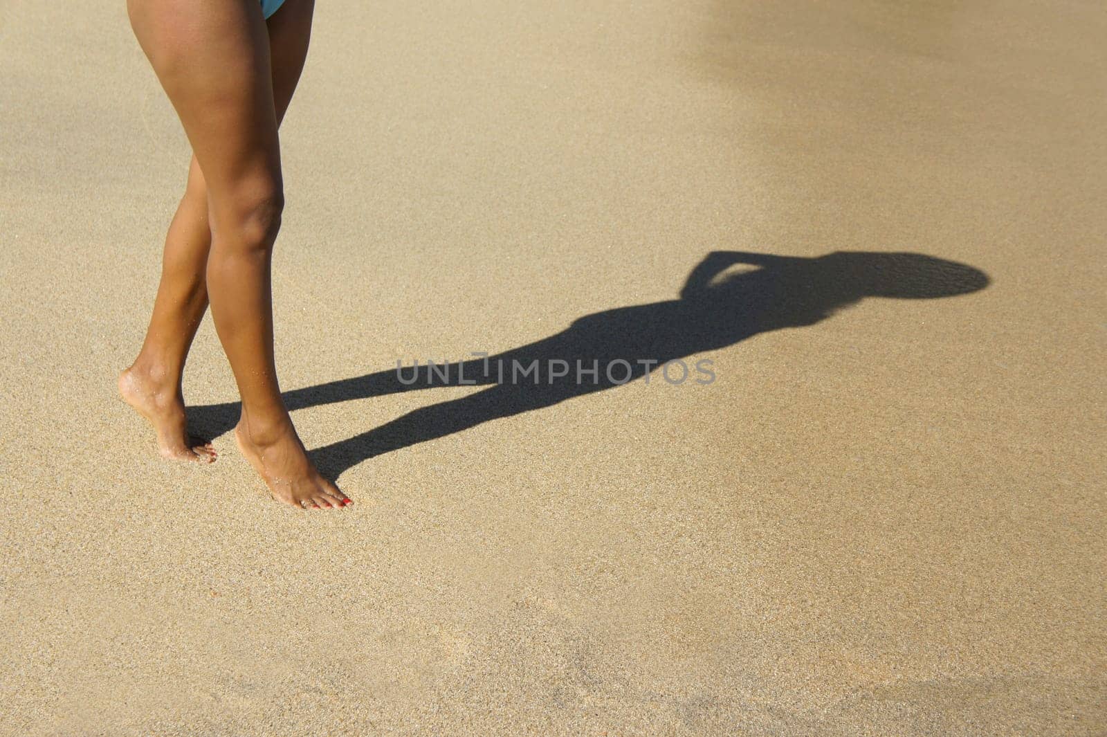 A woman walking on the beach casting a silhouette shadow.