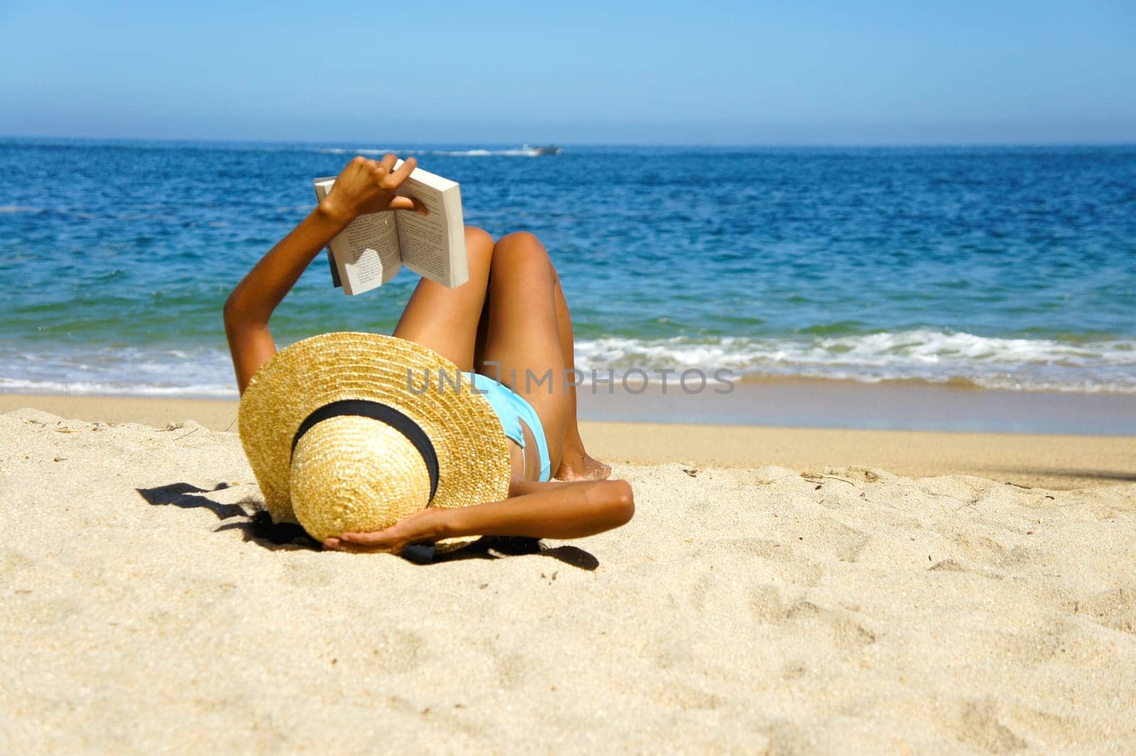 A young woman reading a book on the beach.