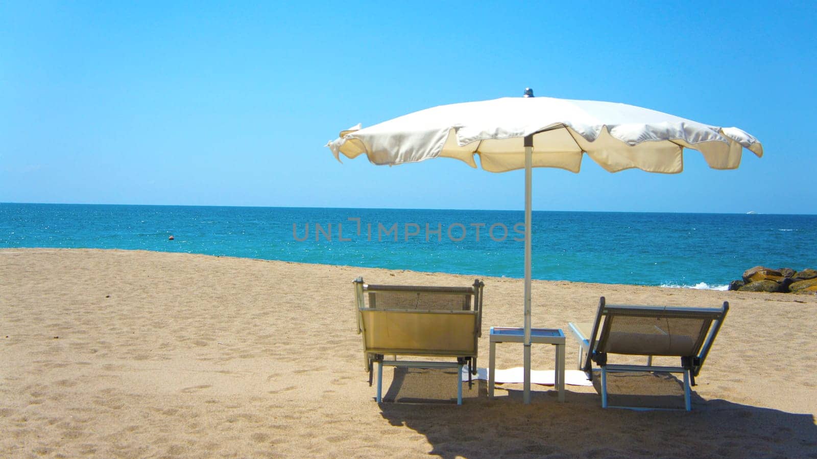 Two chairs a table and a white umbrella on the beach.