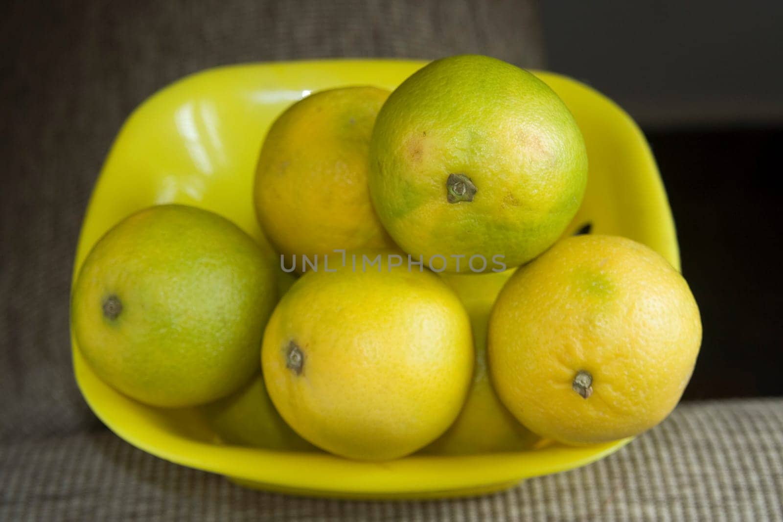 Yellow and greenish sweet lemons placed in yellow plastic tray