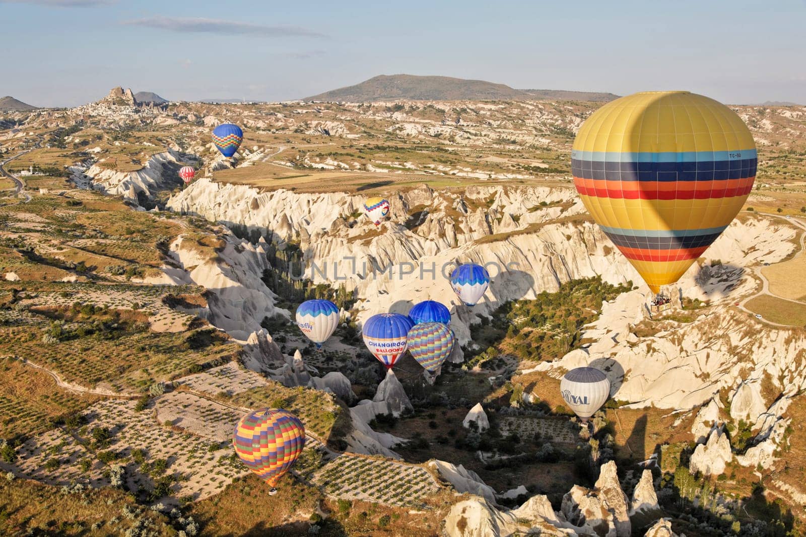 Aerial view of colorful hot air balloons carrying passengers negotiating the surreal terrain of Cappadocia, Turkey though a natural gorge