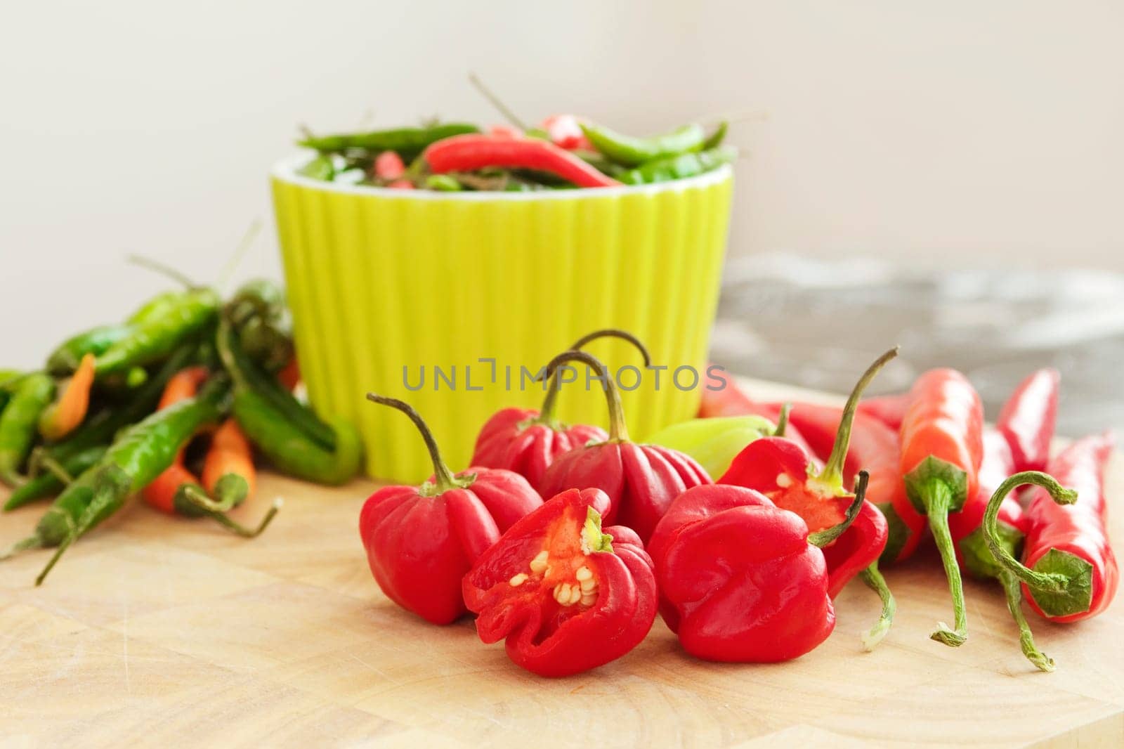A chopping board showing a selection of chilli peppers - bird's eye chillis, red and green chillis, and Scotch bonnet chillis. One of the Scotch bonnet chillis are cut in half, revealing the seeds.