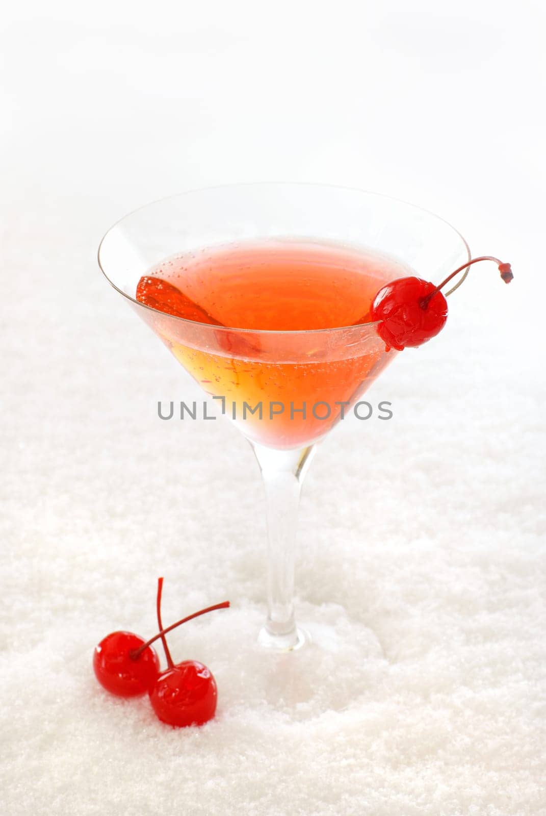 Cherry cocktail in a martini glass decorated with maraschino cherries, on snow.