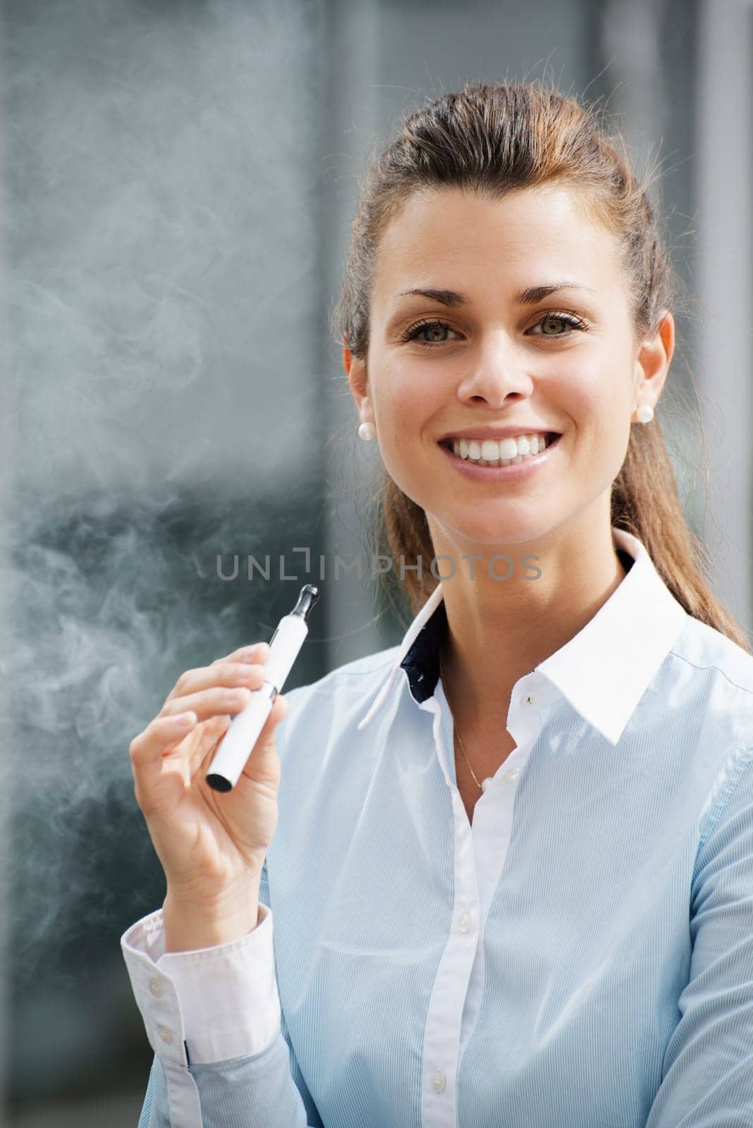 portrait of young female smoker smoking e-cigarette outdoor office building and looking at camera