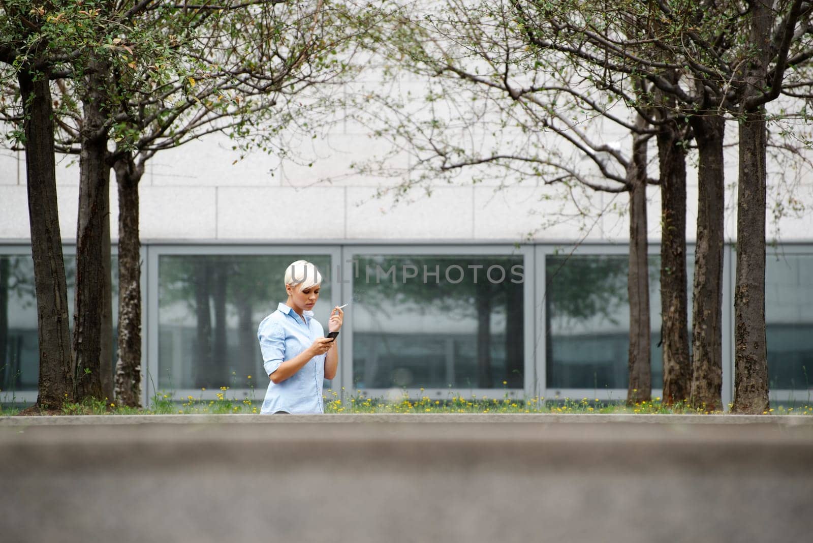 young businesswoman smoking cigarette during break out of office building. Wide shot, copy space