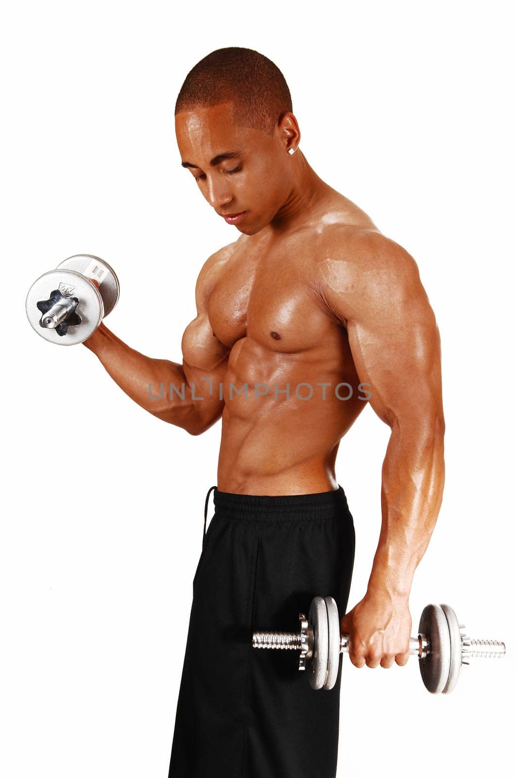 A picture from the side of a young bodybuilder in black shorts lifting.two silver colour dumbbells in his exercises..