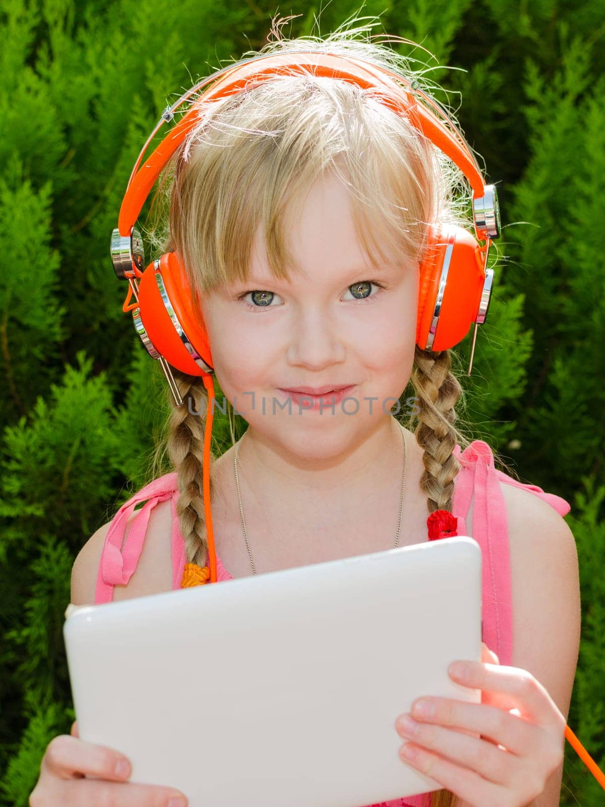 Smiling girl holding tablet pc and listening music in vivid orange headphones