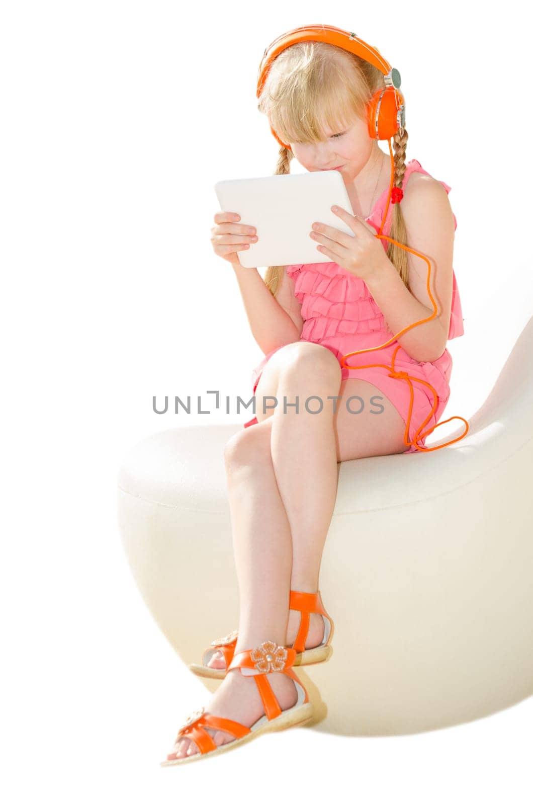 Girl in design armchair holding tablet PC and watching video in orange headphones isolated on white