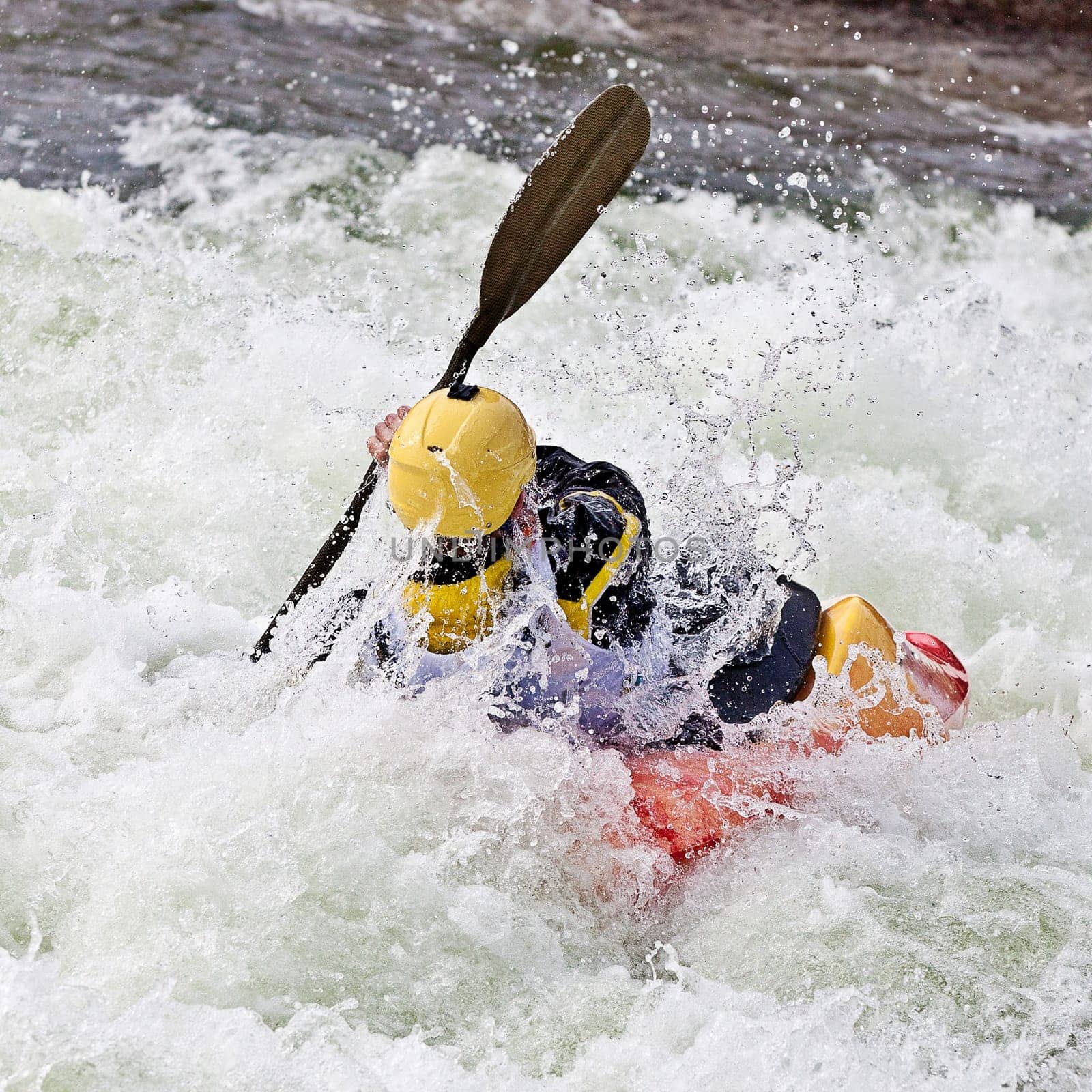 an active male kayaker rolling and surfing in rough water