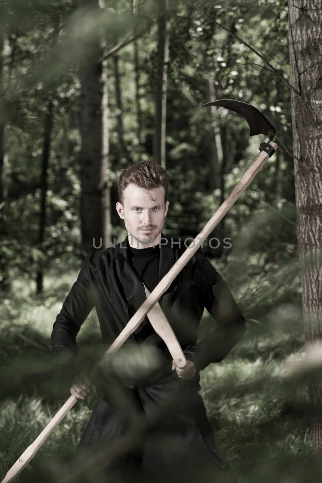 Man with black coat and scythe in the forest