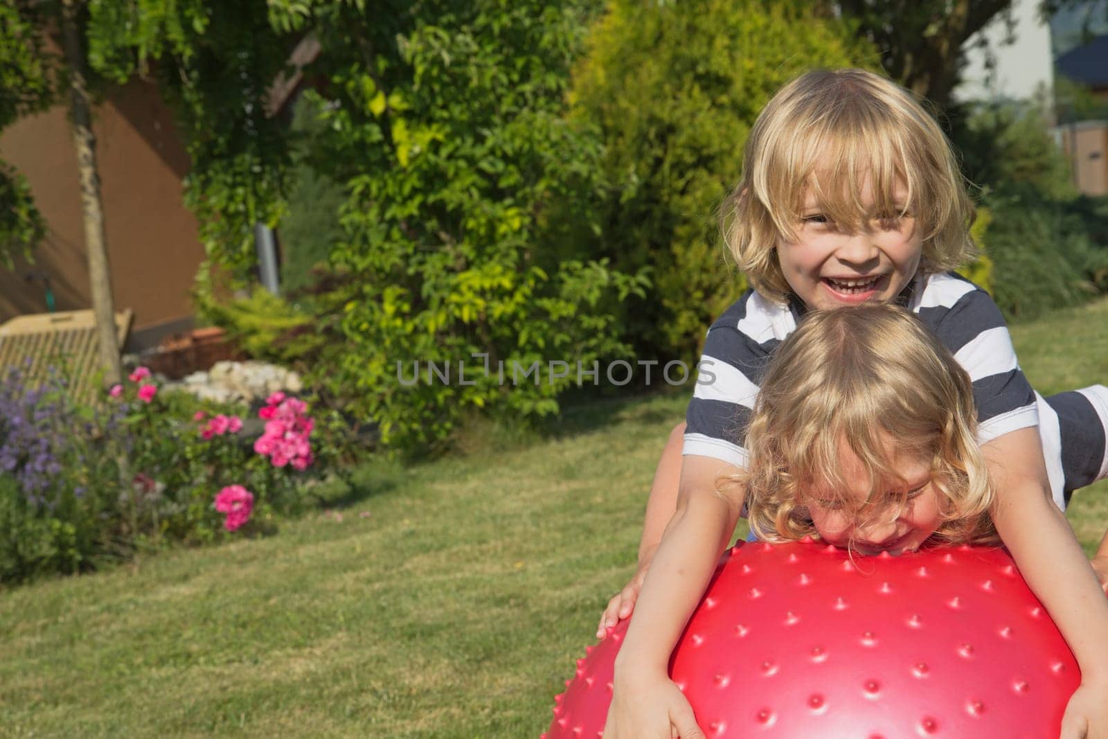 Two attractive blond boys are playing with red gymnastic ball outdoors
