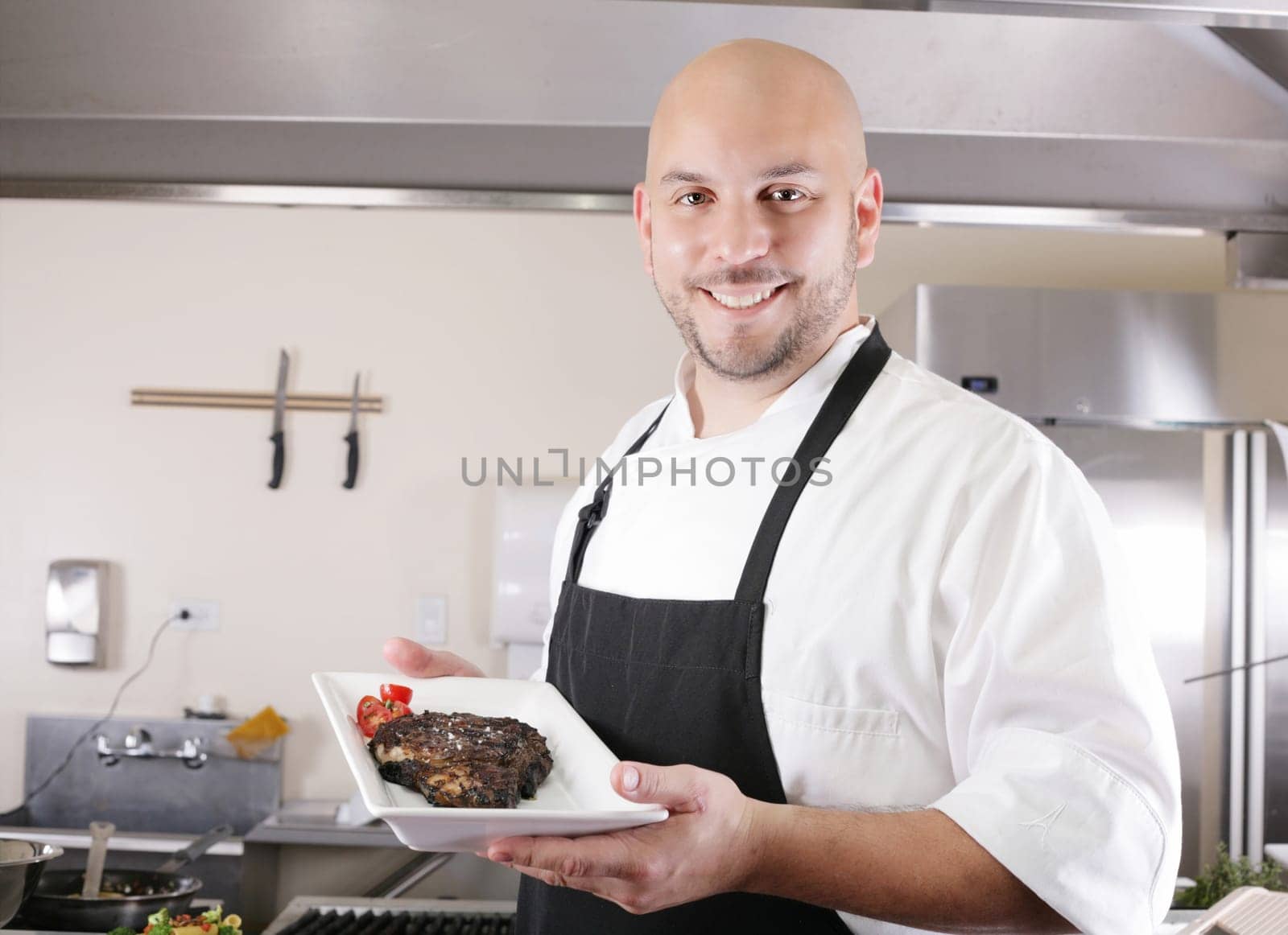 young male chef presenting a juicy ribeye steak with tomatoes