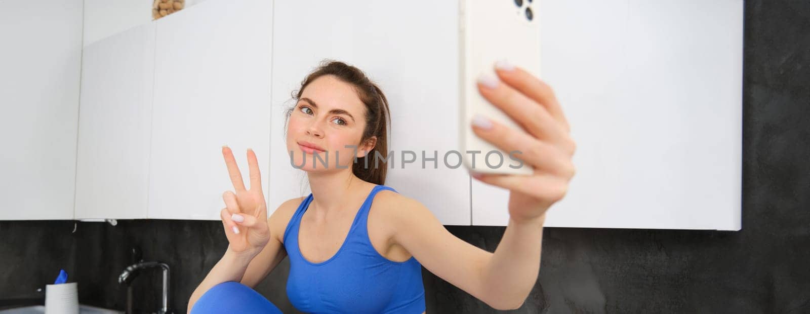 Fit and healthy young sports woman, showing peace sign, taking selfie in activewear, fitness blogger making photos for social media in her activewear by Benzoix