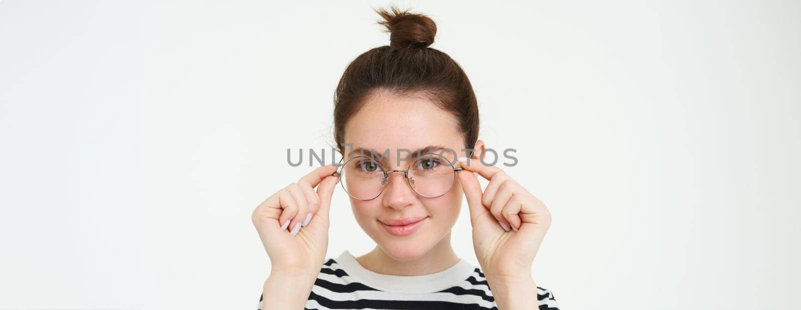 Close up portrait of smiling, attractive young woman wearing new eyewear, trying on glasses for vision, standing over white background.