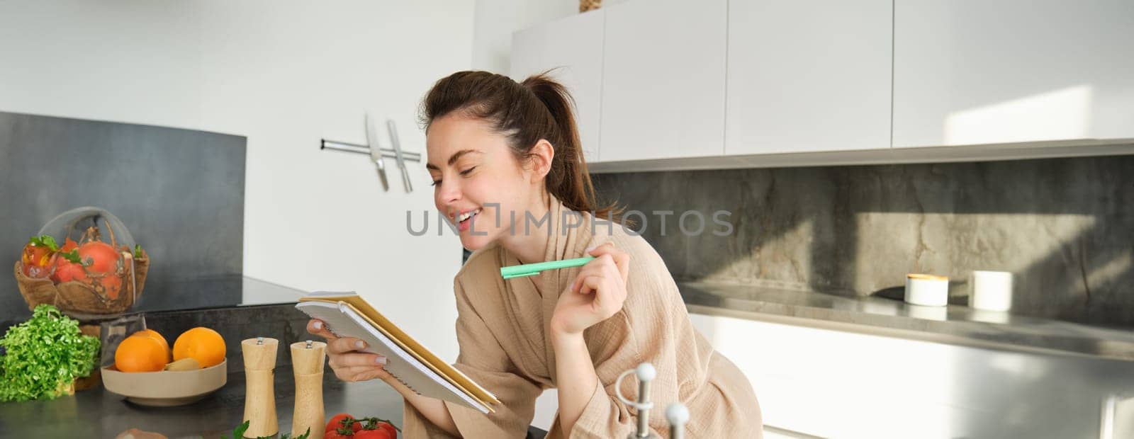 Portrait of woman cooking in the kitchen, reading her notes, checking recipe while preparing meal, making breakfast salad, writing down grocery list by Benzoix