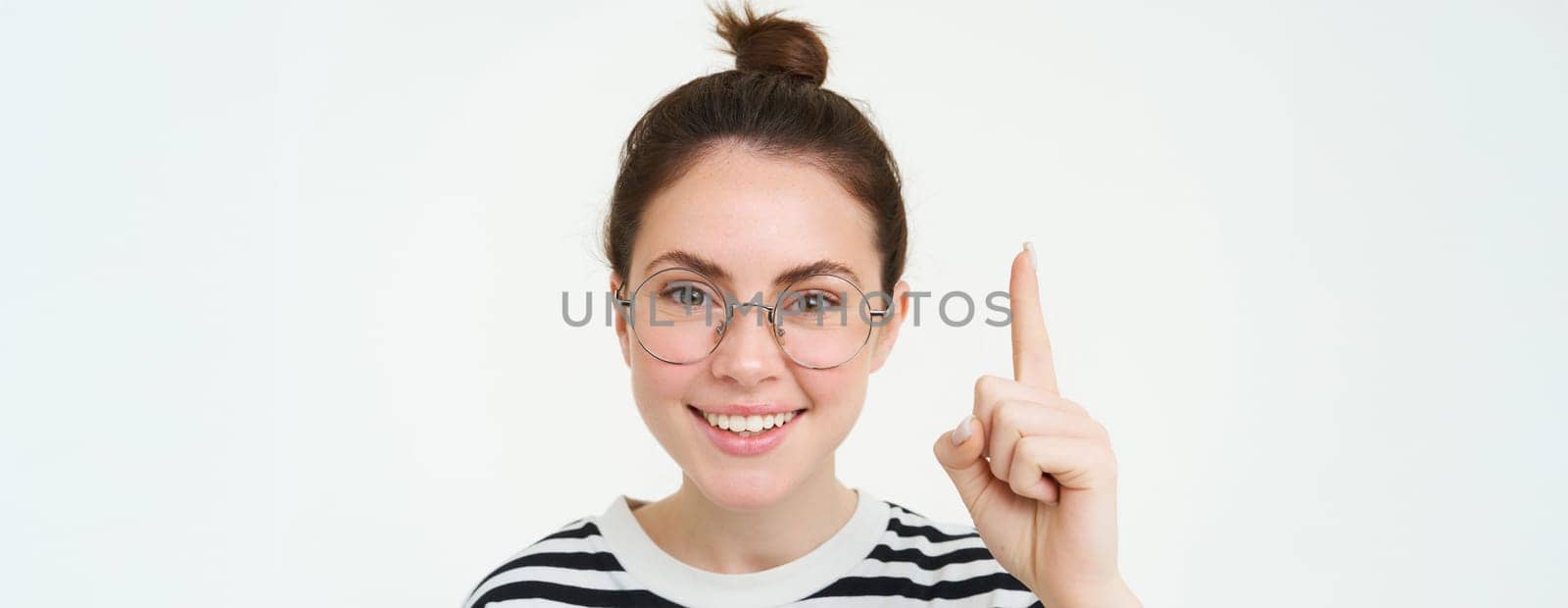 Image of woman in glasses, pointing finger up, showing advertisement on top, standing over white background. Copy space