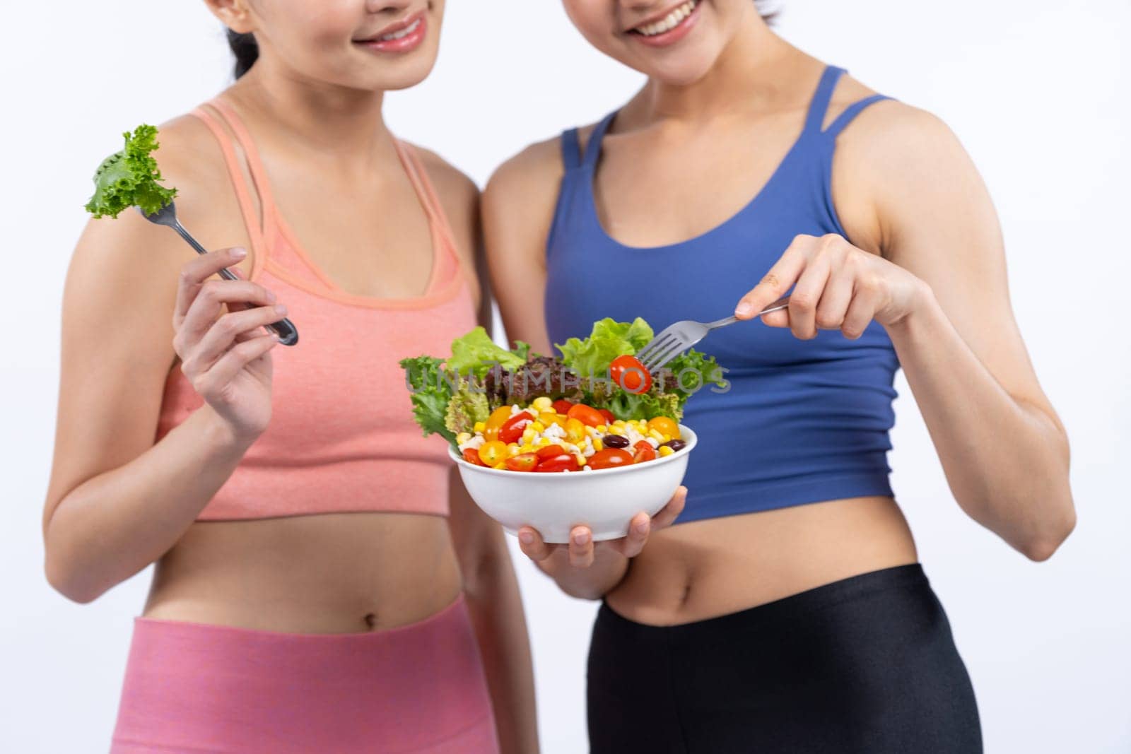 Two young sporty Asian women in sportswear holding salad bowl fill with fruit and vegetable. Natural youthful and fit body lifestyle people with balance nutrition on isolated background. Vigorous