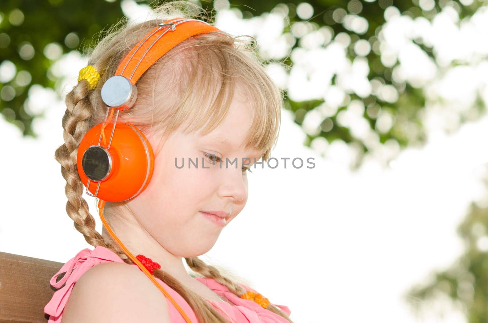 Girl sitting on bench in park and listening language audio course over white and green bokeh background
