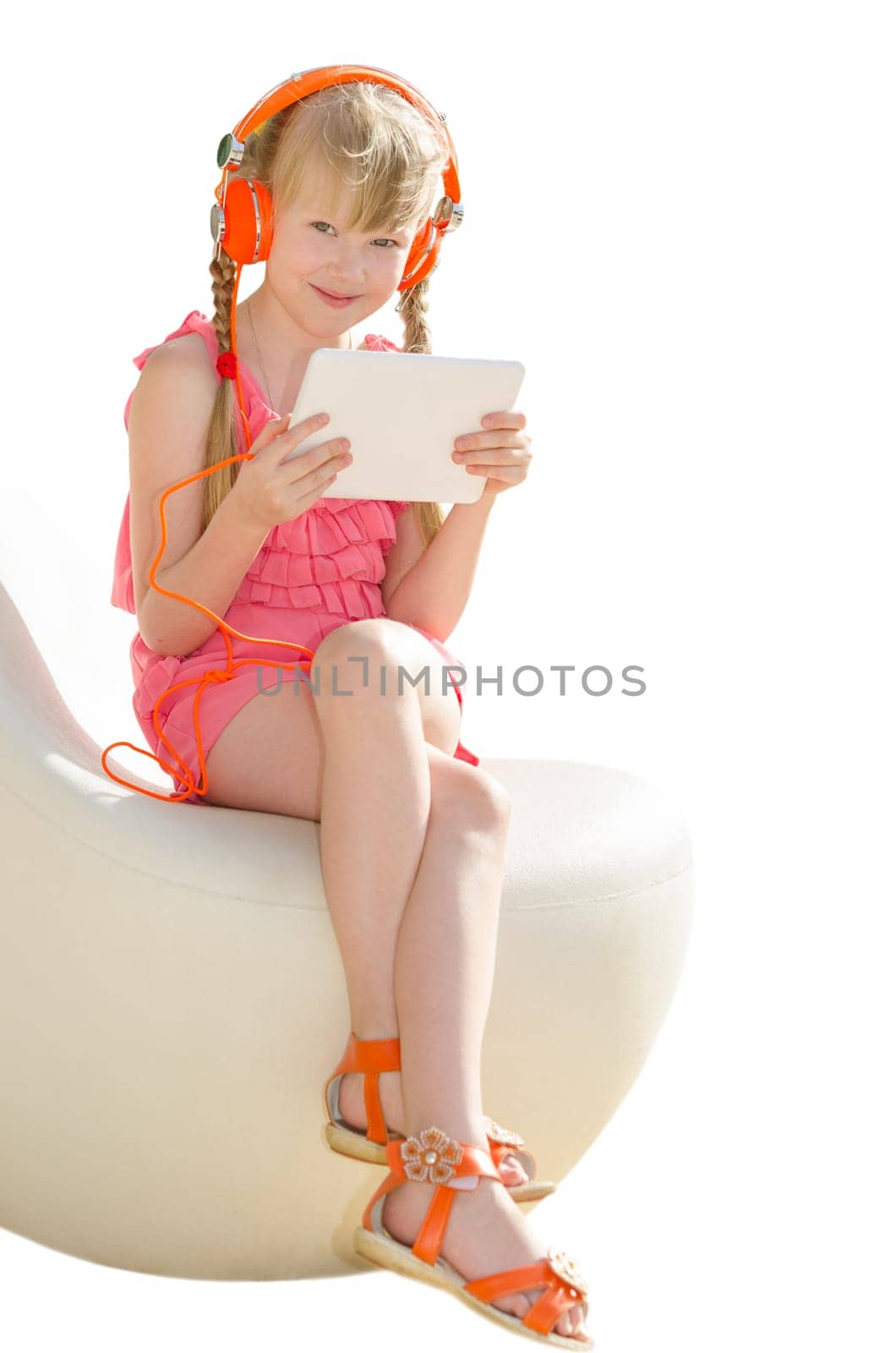 Smiling pretty girl sitting on design armchair with orange headphones and using white tablet pc isolate