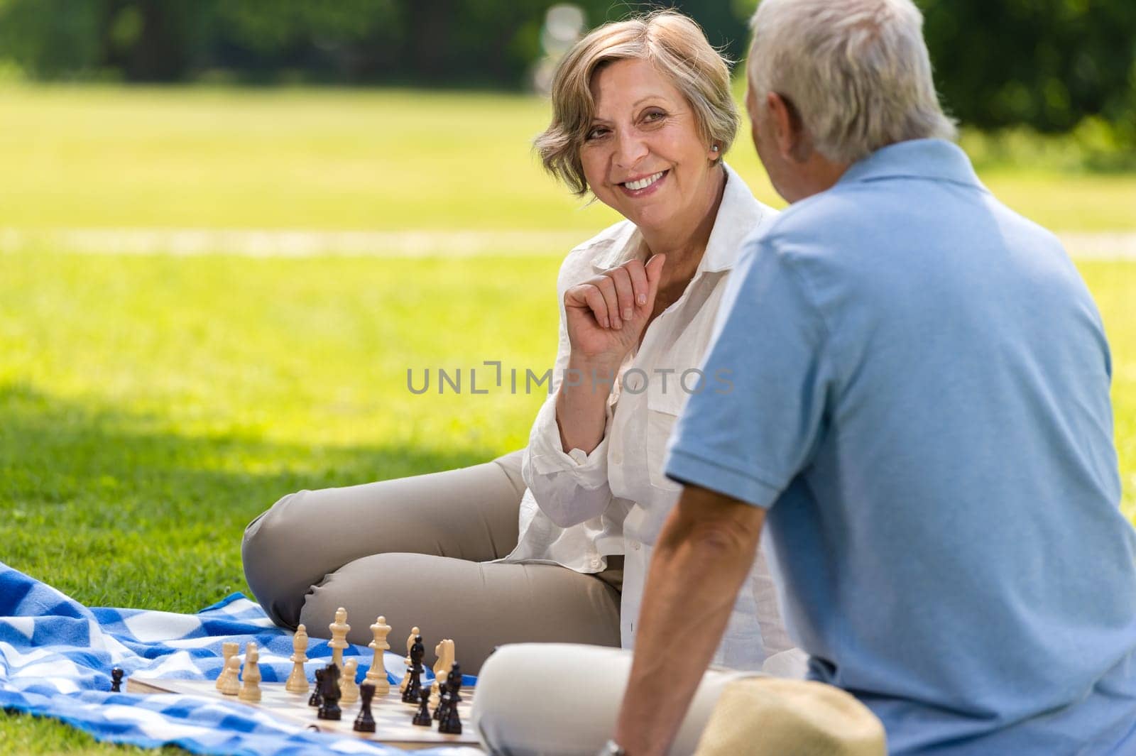 Senior wife and husband playing chess on blanket summer park