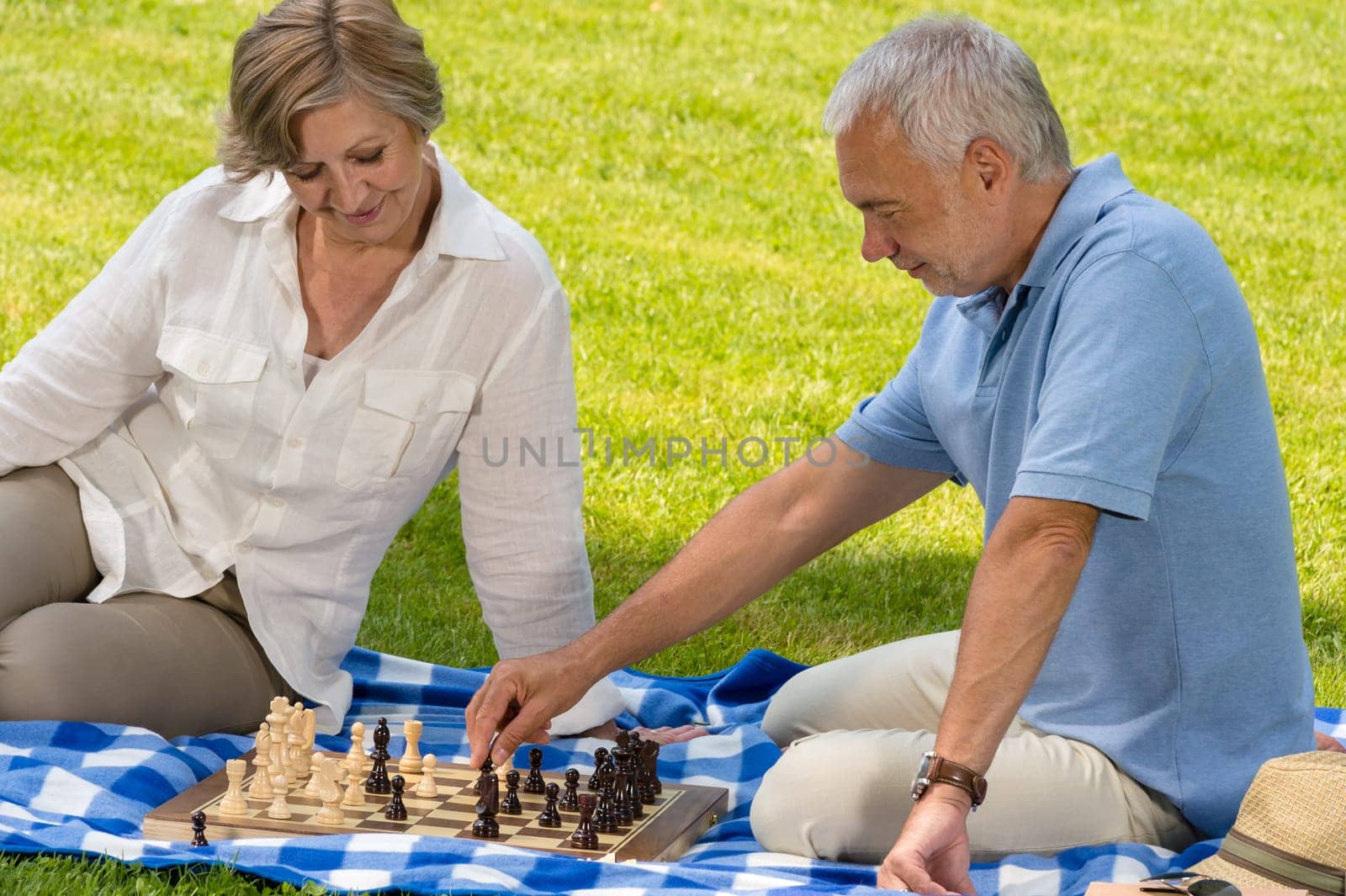 Retired senior couple playing chess in park sitting blanket grass