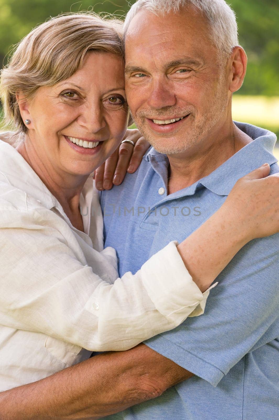 Senior couple hugging and smiling in park looking at camera