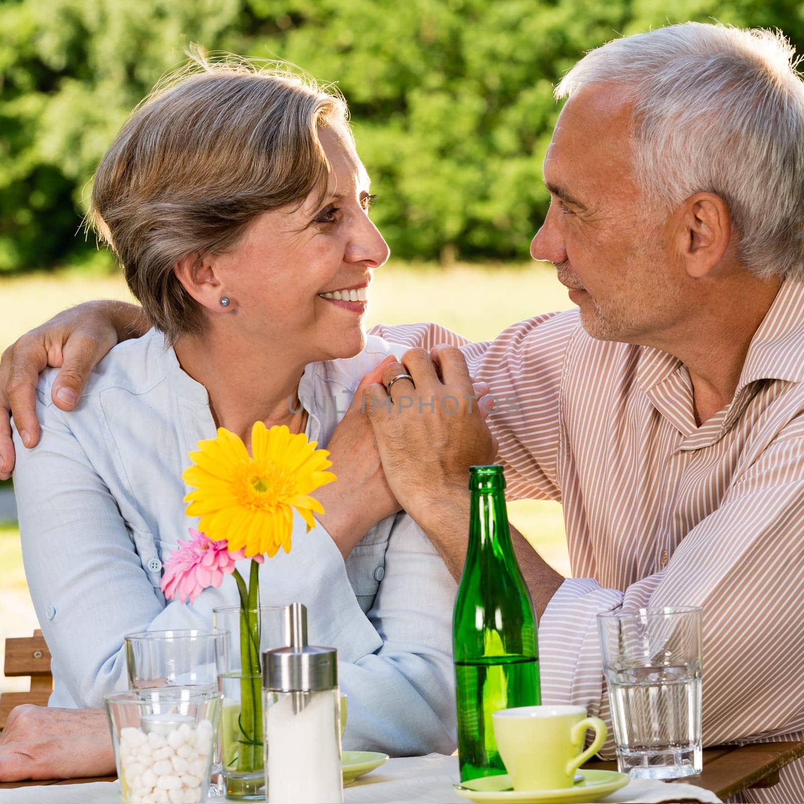 Retired couple sitting at table holding hands outdoors