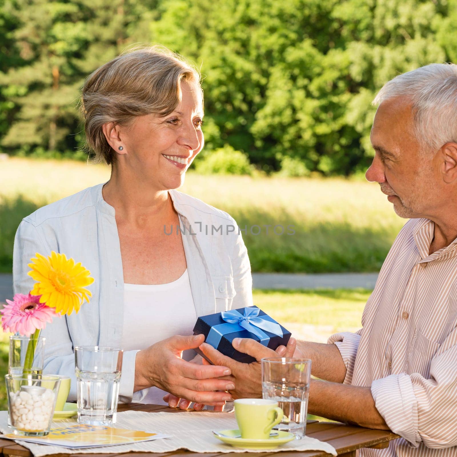 Senior woman giving husband anniversary gift in park