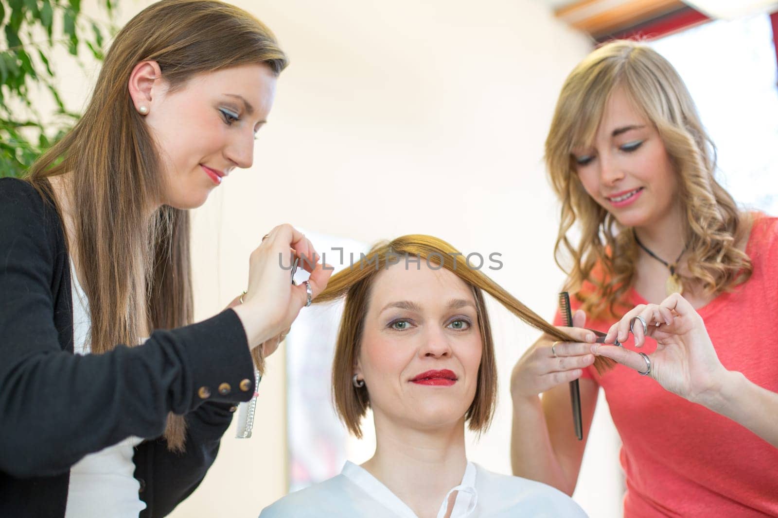 Two hairdressers with comb and scissors with a customer at work
