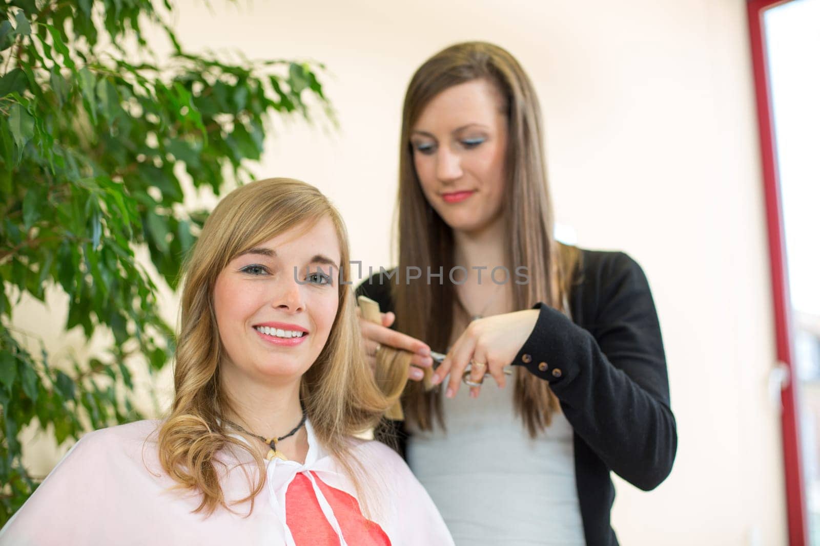 Happy customer getting her hair cut by hairdresser or stylist in salon