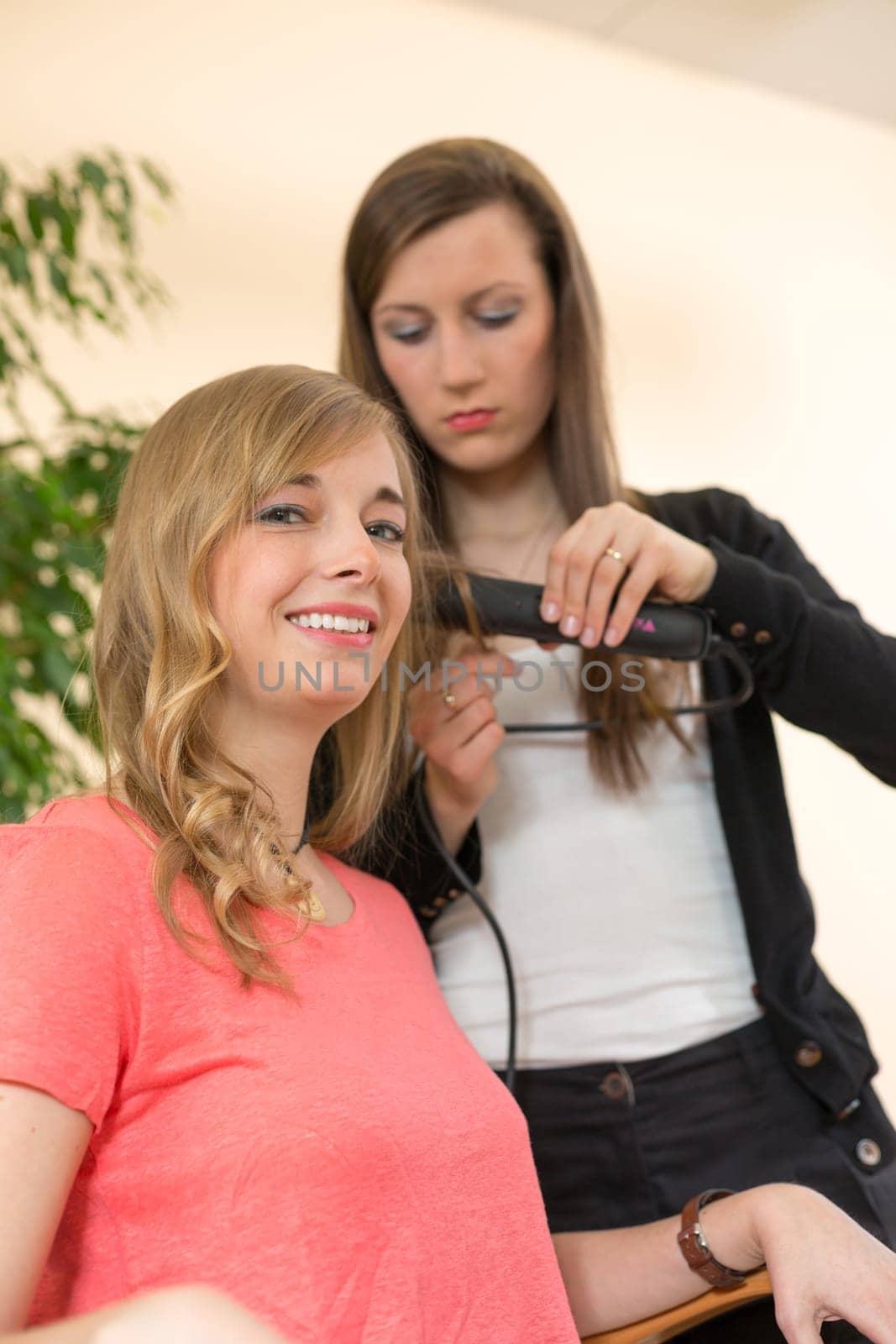 Hairdresser in salon making locks for a customer with a hair straightener