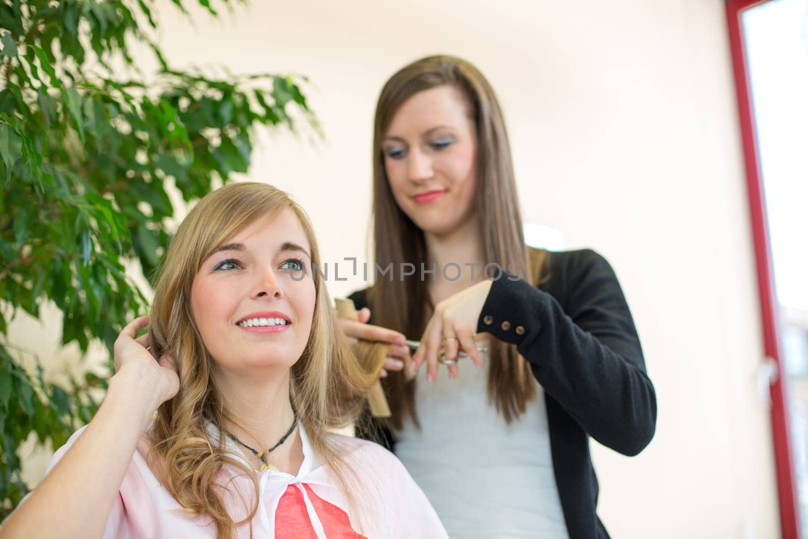 Happy customer getting her hair cut by hairdresser or stylist in salon