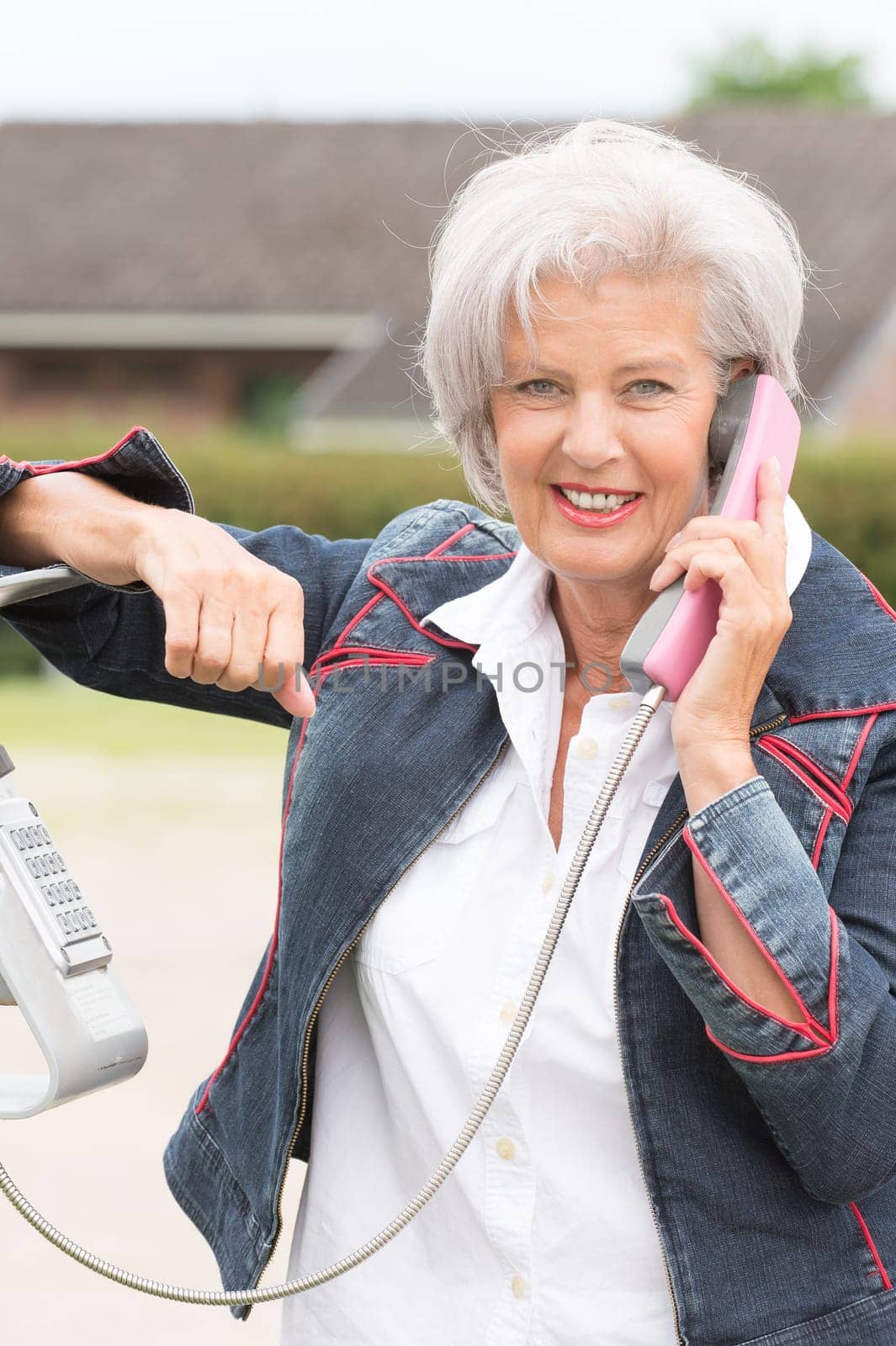 Smiling elderly woman at a telephone booth