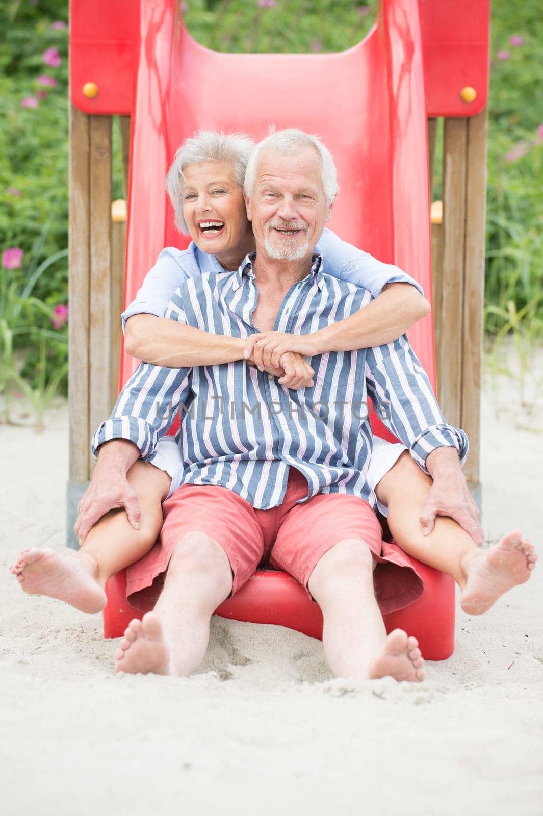 Happy senior couple on the beach on a children's slide