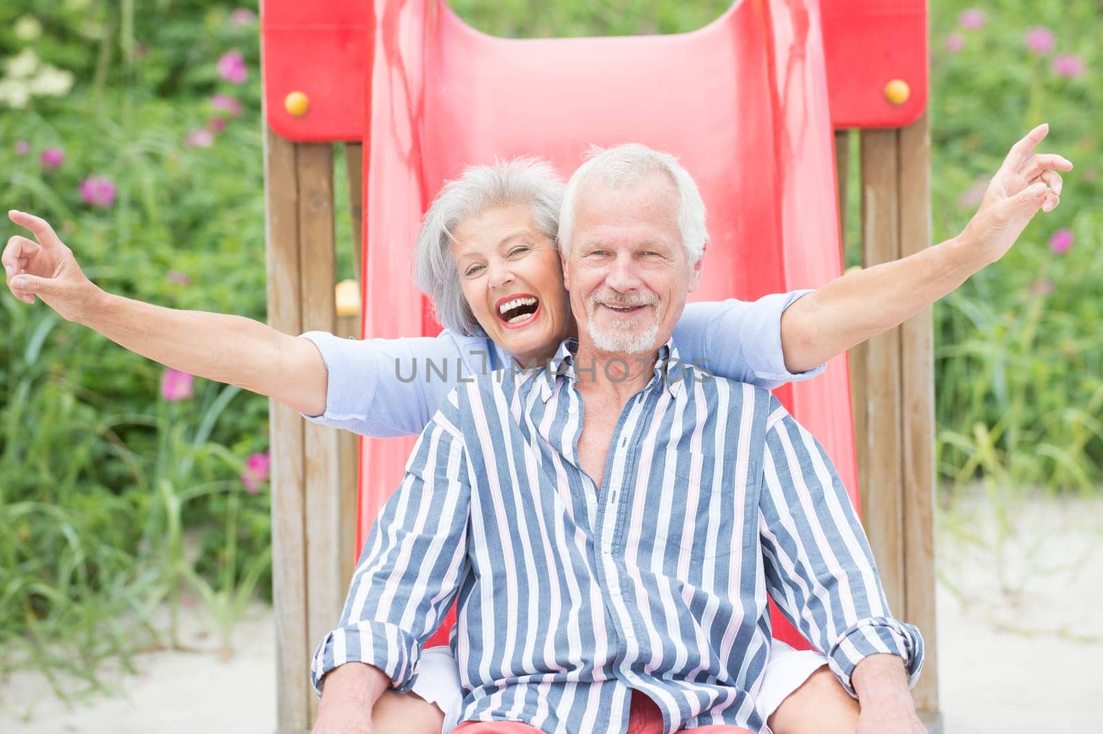 Happy senior couple on the beach on a children's slide