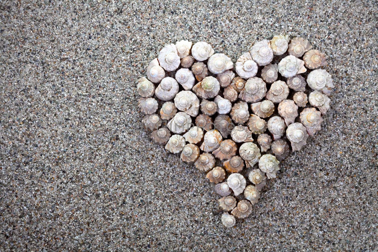 Sea shells heart on sandy beach background. Summer composition with copy space. Top view.